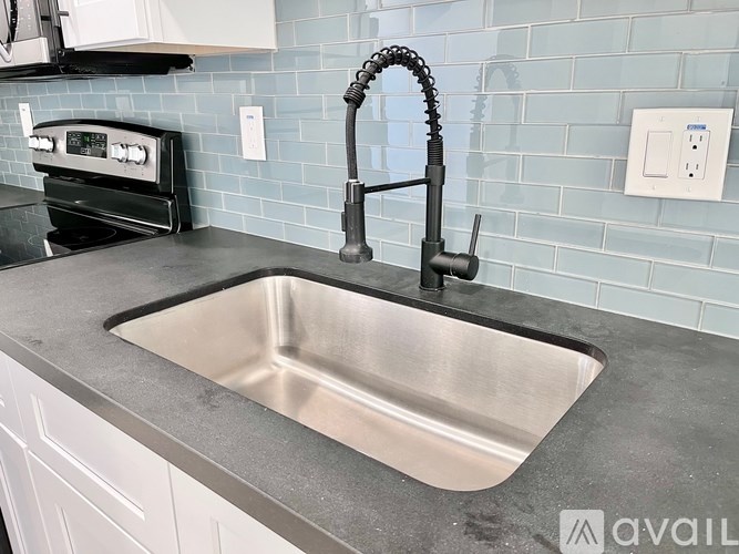 A kitchen sink with a black faucet and a blue tile backsplash.