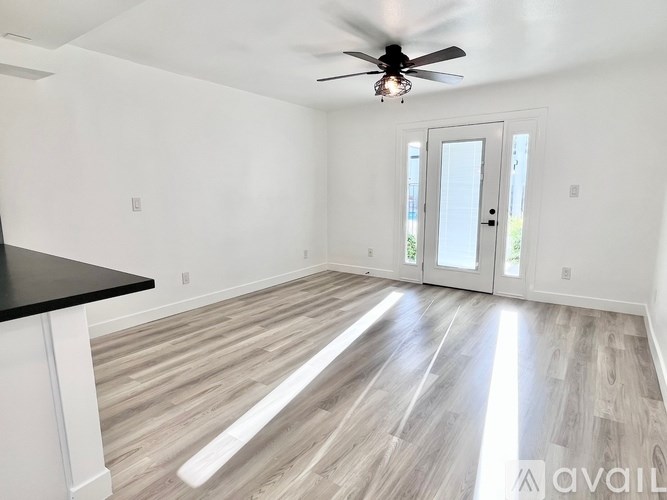A spacious room with a ceiling fan and light, hardwood floors, and a black countertop with white cabinetry.