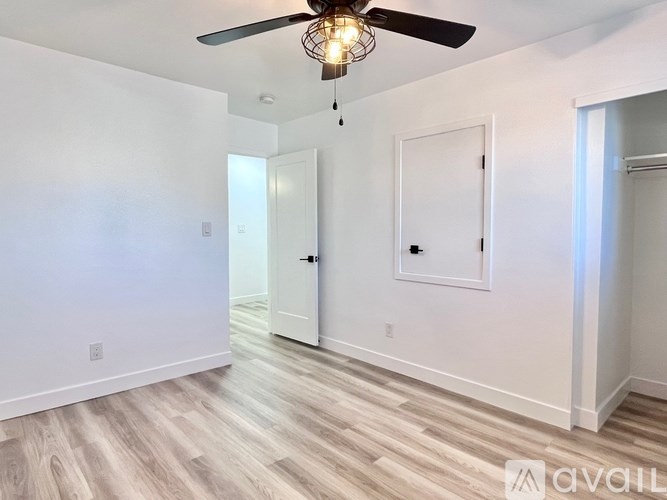 A room with a ceiling fan and light fixture, two doors, and a wooden floor.