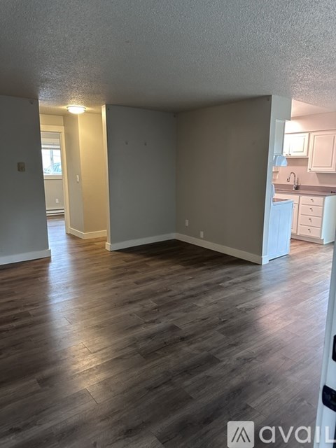 A room with wooden flooring and a kitchen in the background.