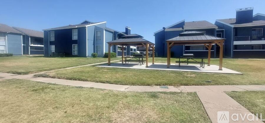 A gazebo sits in the middle of a grassy area in front of apartment buildings.