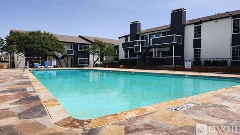 A swimming pool surrounded by a stone patio and a building in the background.