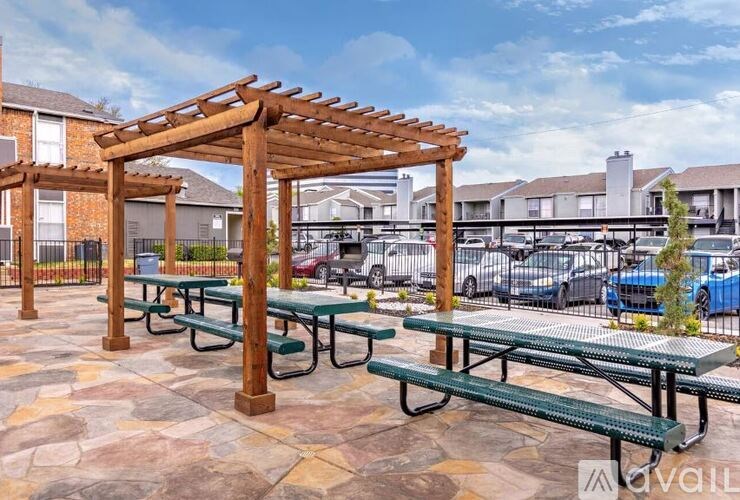 A wooden pergola with green benches is in the foreground of a parking lot.