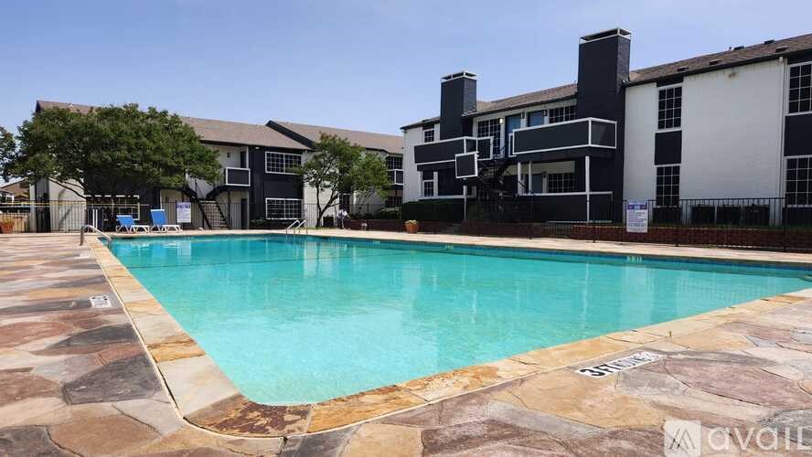A swimming pool surrounded by a stone patio and a building in the background.