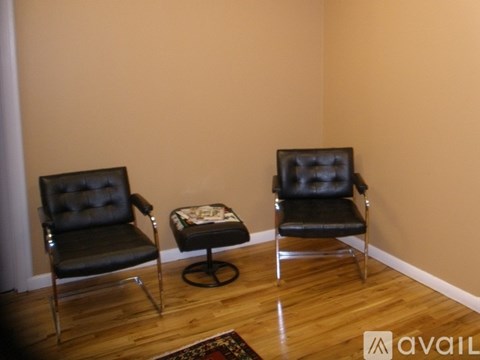 Two black chairs and a small ottoman are in a room with wooden floors.