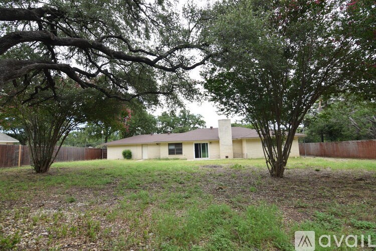 A house is available for sale, surrounded by trees and a fence.