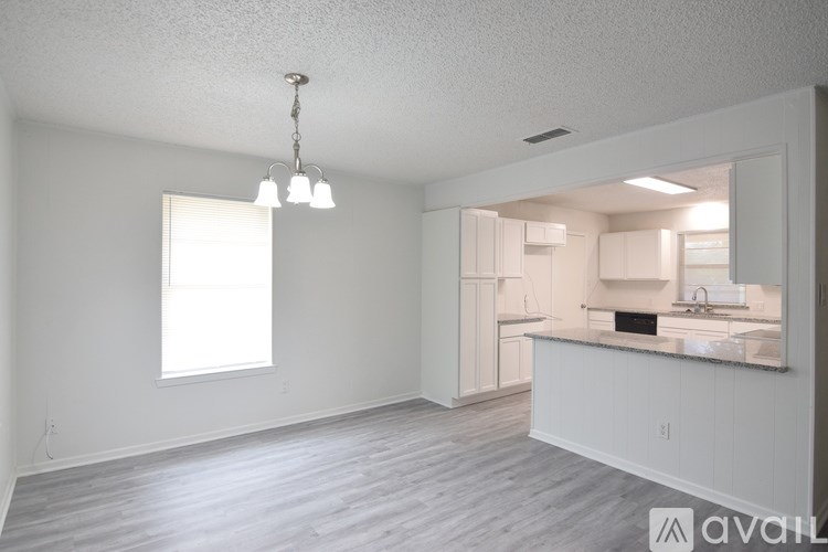 A spacious room with a window and a kitchen area with white cabinets and a sink.