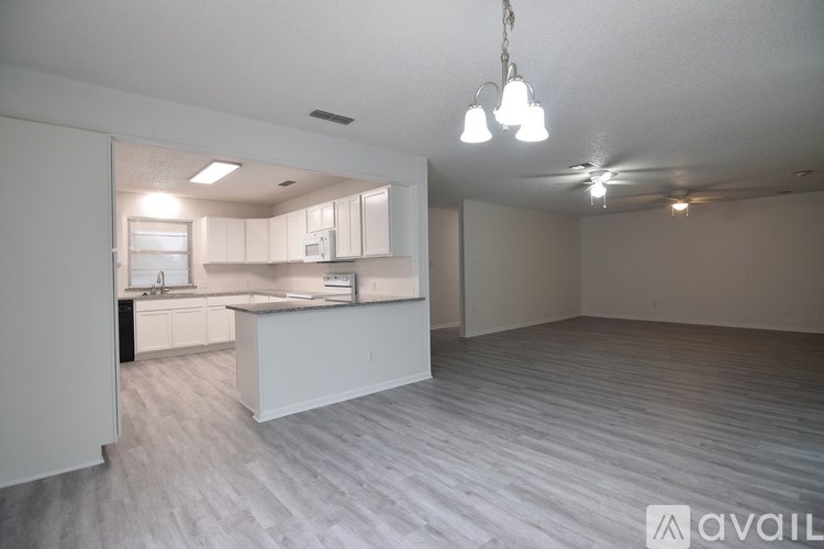 A spacious kitchen and living room with a white countertop and light wood flooring.