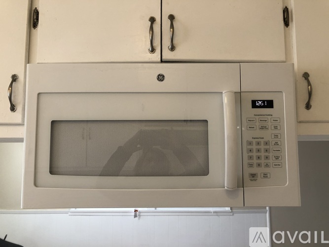 A microwave oven with a digital display and control panel is mounted on a kitchen cabinet.
