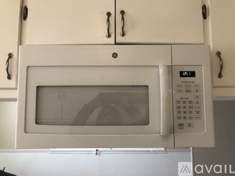 A microwave oven with a digital display and control panel is mounted on a kitchen cabinet.