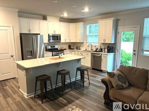 A kitchen with white cabinets and a white island with a refrigerator, microwave, and stove.