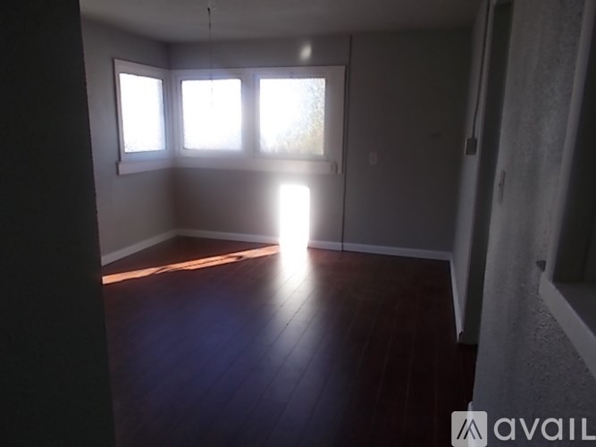 A room with wooden floors and two windows letting in sunlight.