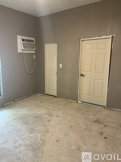 A room with a white door and a window with a wall-mounted air conditioner unit.