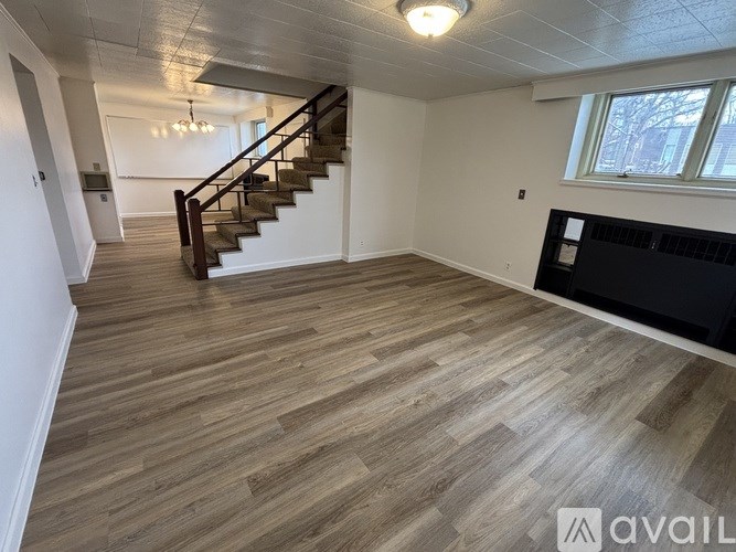 A spacious room with wooden flooring and a staircase.