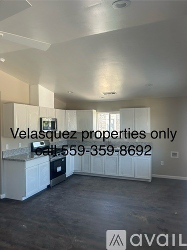 A spacious, empty room with a kitchen area and a phone number for Velasquez properties.