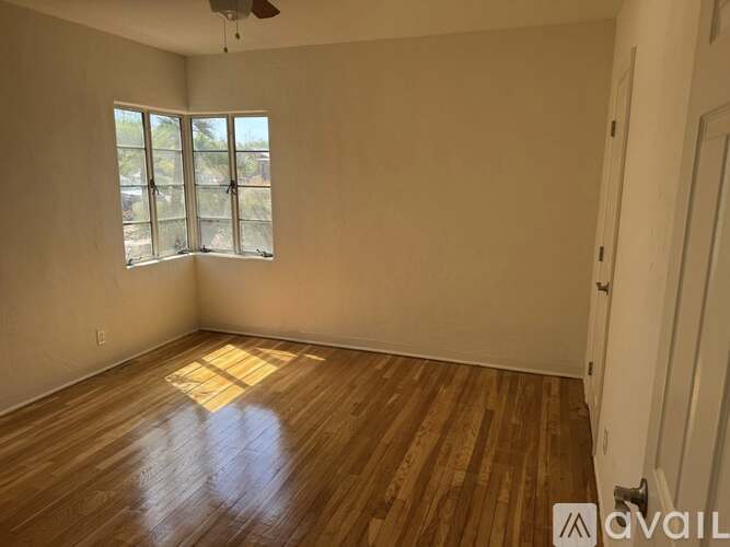 A room with wooden flooring and a window with a view of trees.