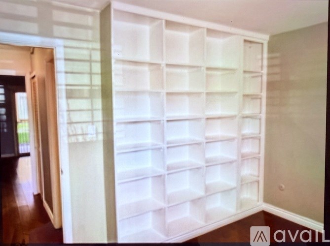 A white shelving unit with multiple compartments is in a room with a wooden floor.