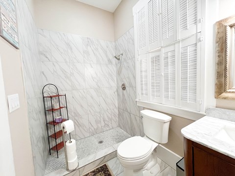 A white toilet sits in a bathroom with a marble tile shower.