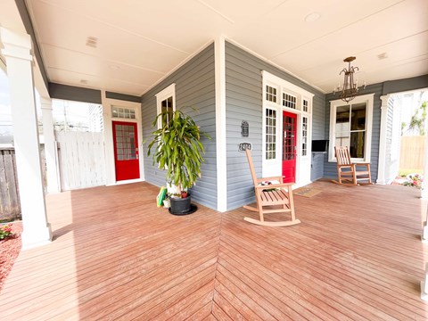 A wooden rocking chair is on a porch with a red door.