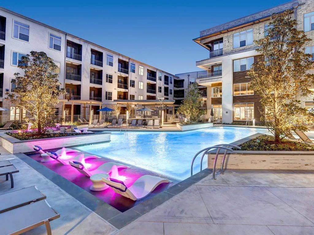 A swimming pool with purple lighting in the middle of a courtyard surrounded by buildings.