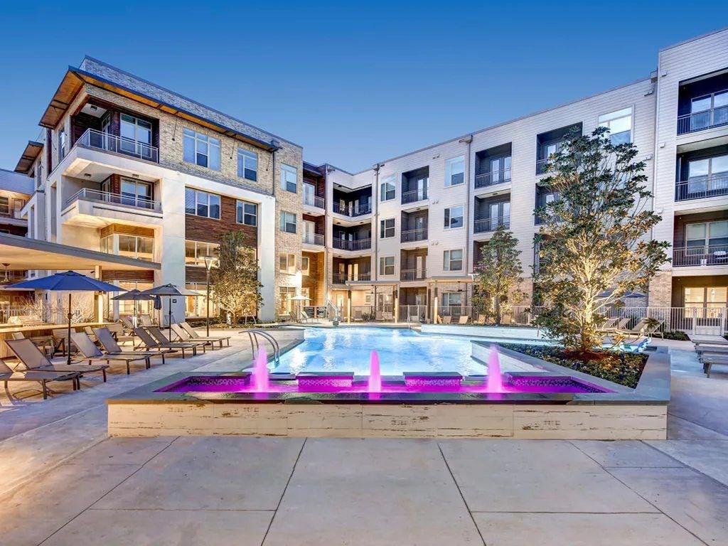A modern apartment complex with a pool and fountain in the courtyard.