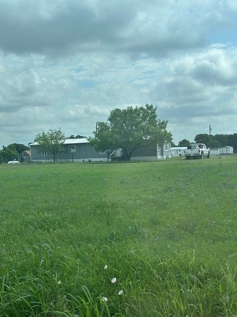 A grassy field with a house and trees in the background.