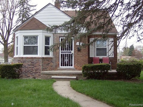 A small house with a white front and a brick wall.
