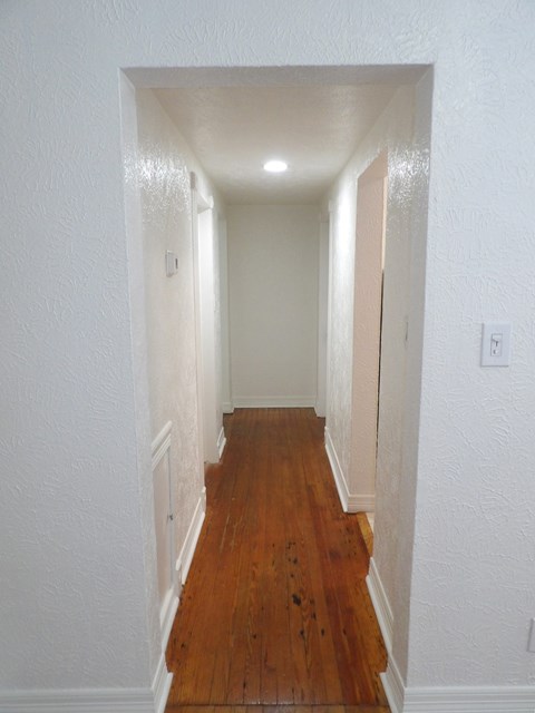 A long hallway with wood floors and white walls.