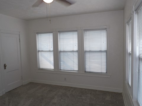 A room with a carpeted floor and three windows.