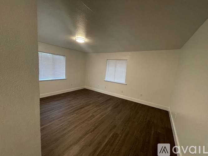 A room with wooden flooring and two windows.