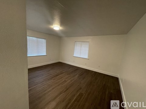 A room with wooden flooring and two windows.