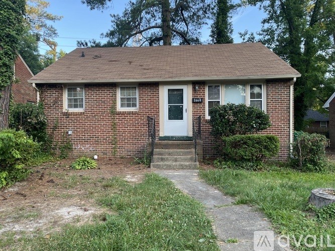 A small red brick house with a white door and a small front yard.