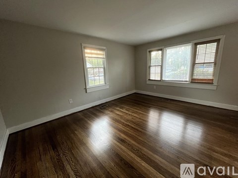 A room with wooden flooring and two windows.