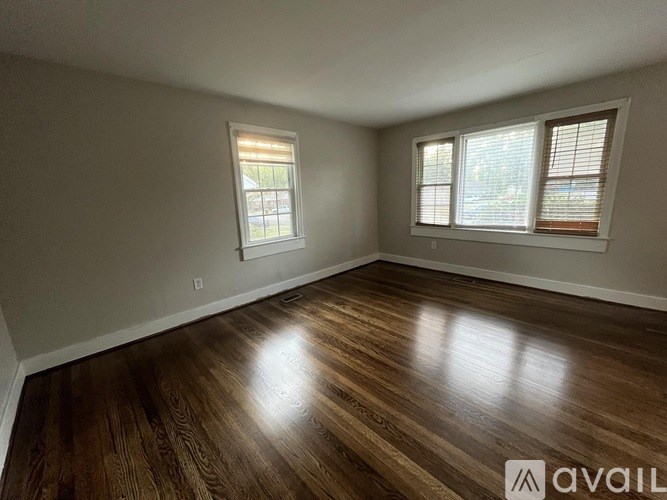 A room with wooden flooring and two windows.