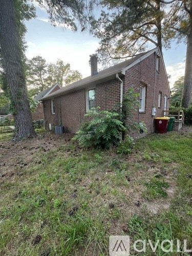A house with a red brick exterior and a chimney is surrounded by trees and vegetation.