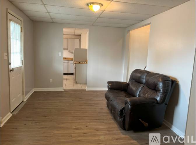 A black leather couch sits in a room with wooden floors and white walls.