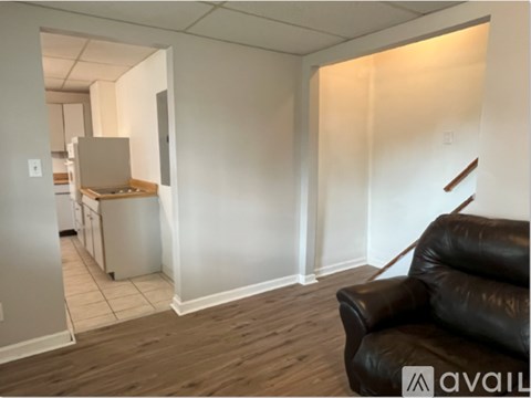 A living room with a black leather couch and a kitchen in the background.
