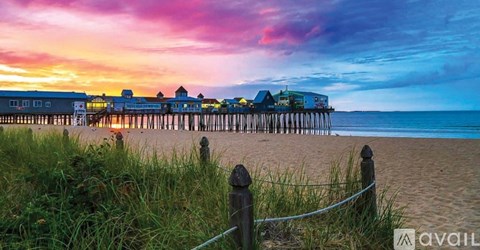 A beach scene with a pier and buildings in the distance during sunset.