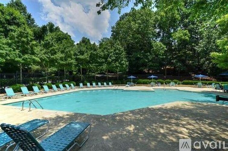 A pool surrounded by trees and lounge chairs.
