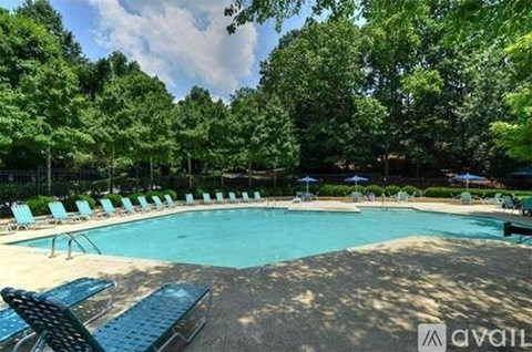 A pool surrounded by trees and lounge chairs.