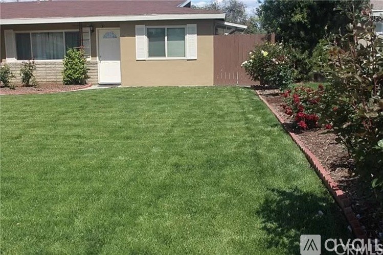 A house with a brown roof and a white door is surrounded by a green lawn.