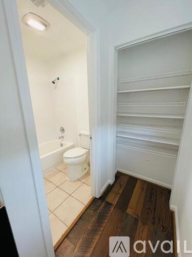 A white toilet is in a small bathroom with wood flooring.