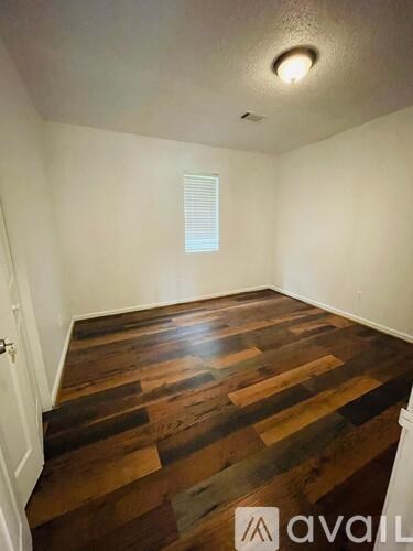 A room with wooden flooring and a window with blinds.