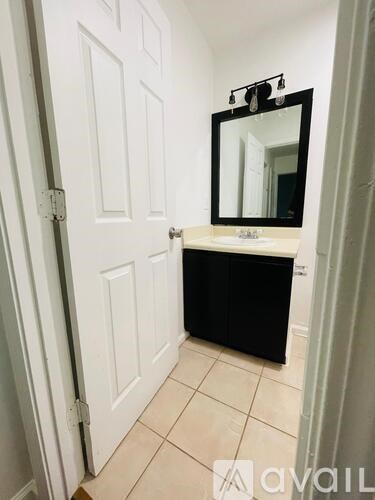 A bathroom with a white door, a sink with a mirror above it and a black cabinet.
