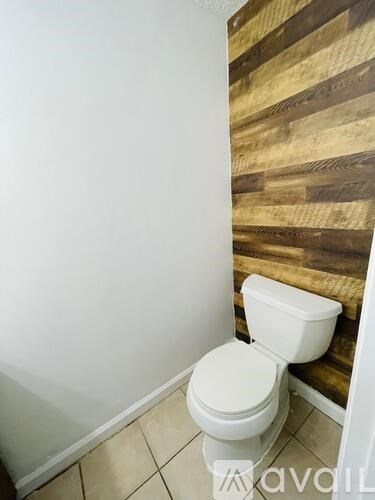 A white toilet in a small bathroom with a wooden wall.