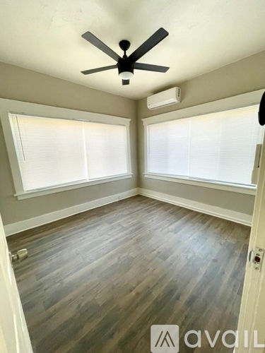 A room with a ceiling fan and two windows.