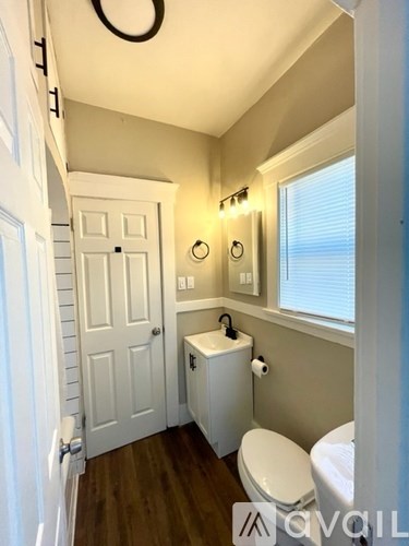 A small white bathroom with wood floors and a toilet.
