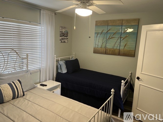 A bedroom with a bed, a fan, and a painting on the wall.