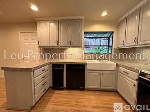 A kitchen with white cabinets and a window overlooking a fence.