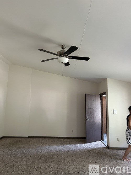 A woman stands in a room with a ceiling fan and a closed door.